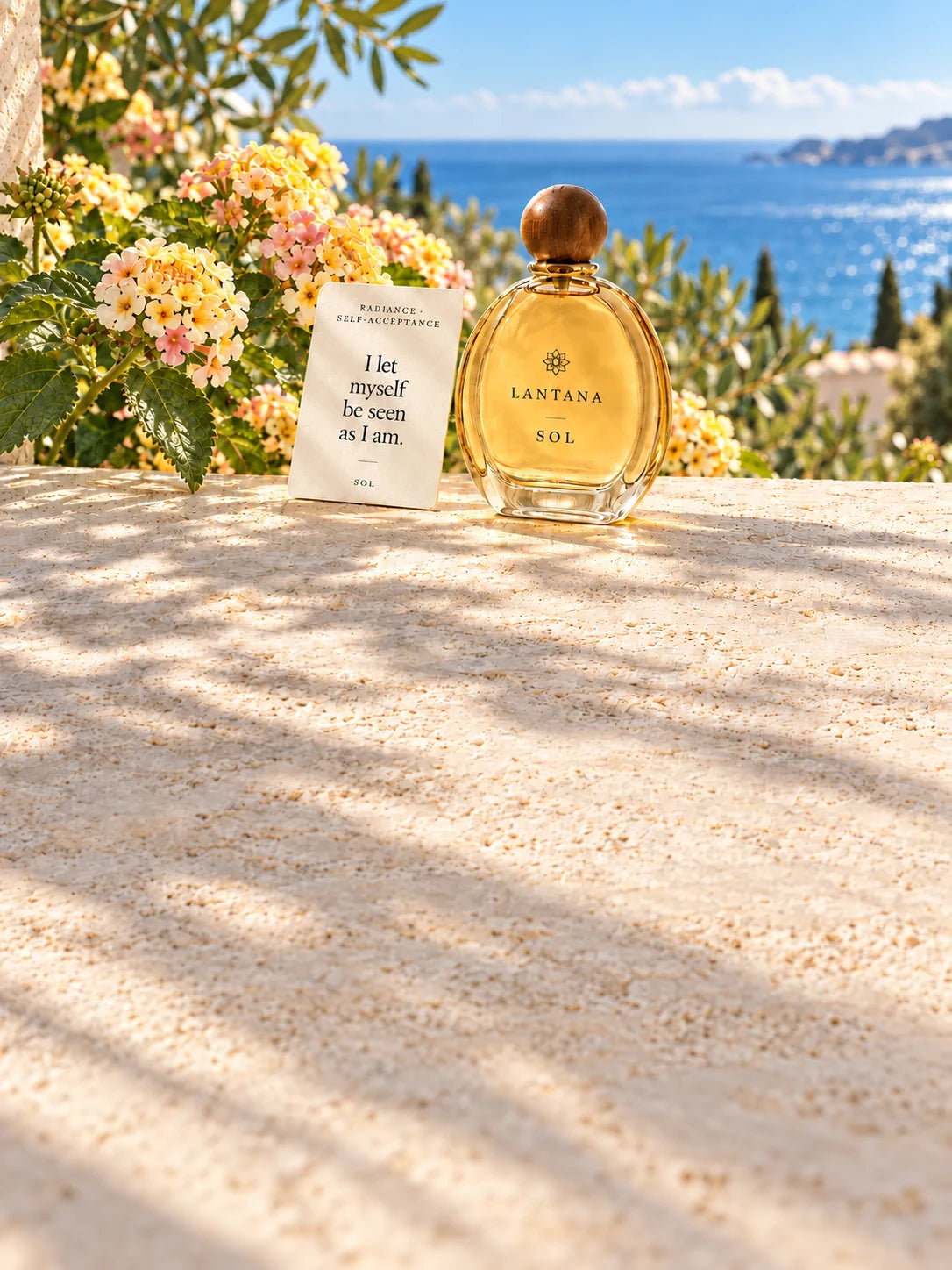 SOL perfume bottle and its Radiance and Self-Acceptance intention card with pale yellow lantana on a sunlit terrace overlooking the Mediterranean.